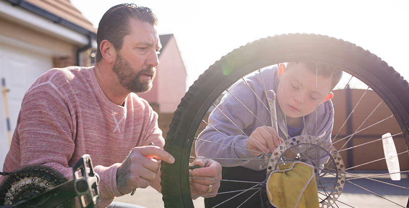 Man and boy fixing a bike, spokes of a wheel in the foreground